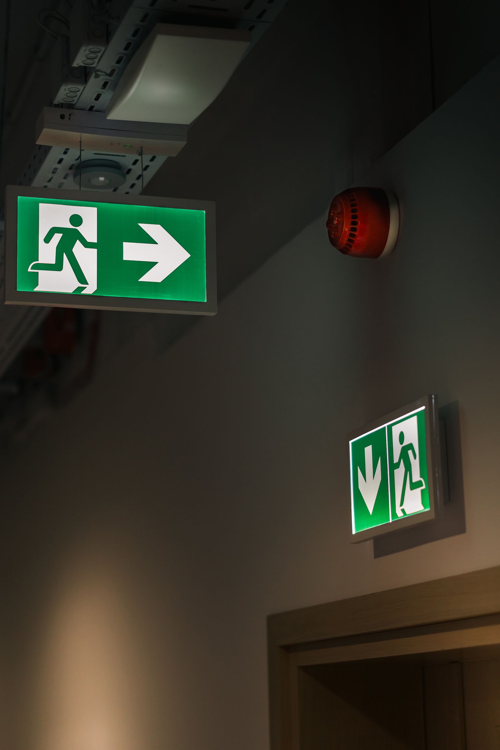 Escape route signage and fire alarm sounder above a timber doorway